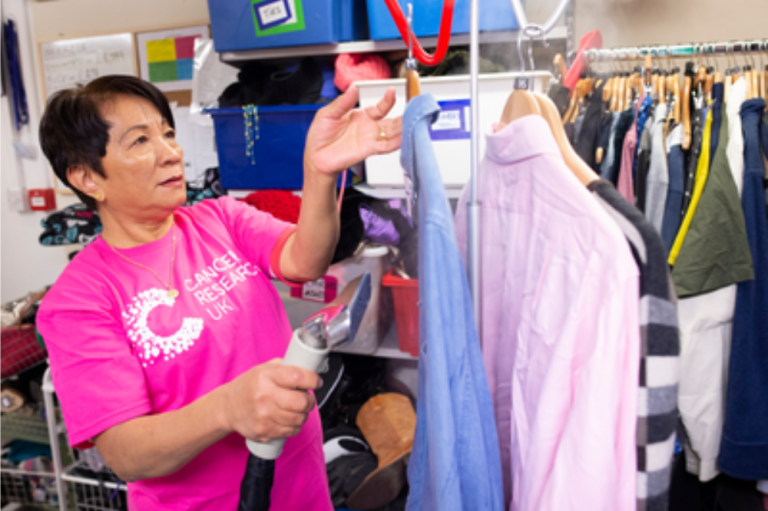 Cancer Research charity store worker steaming shirts